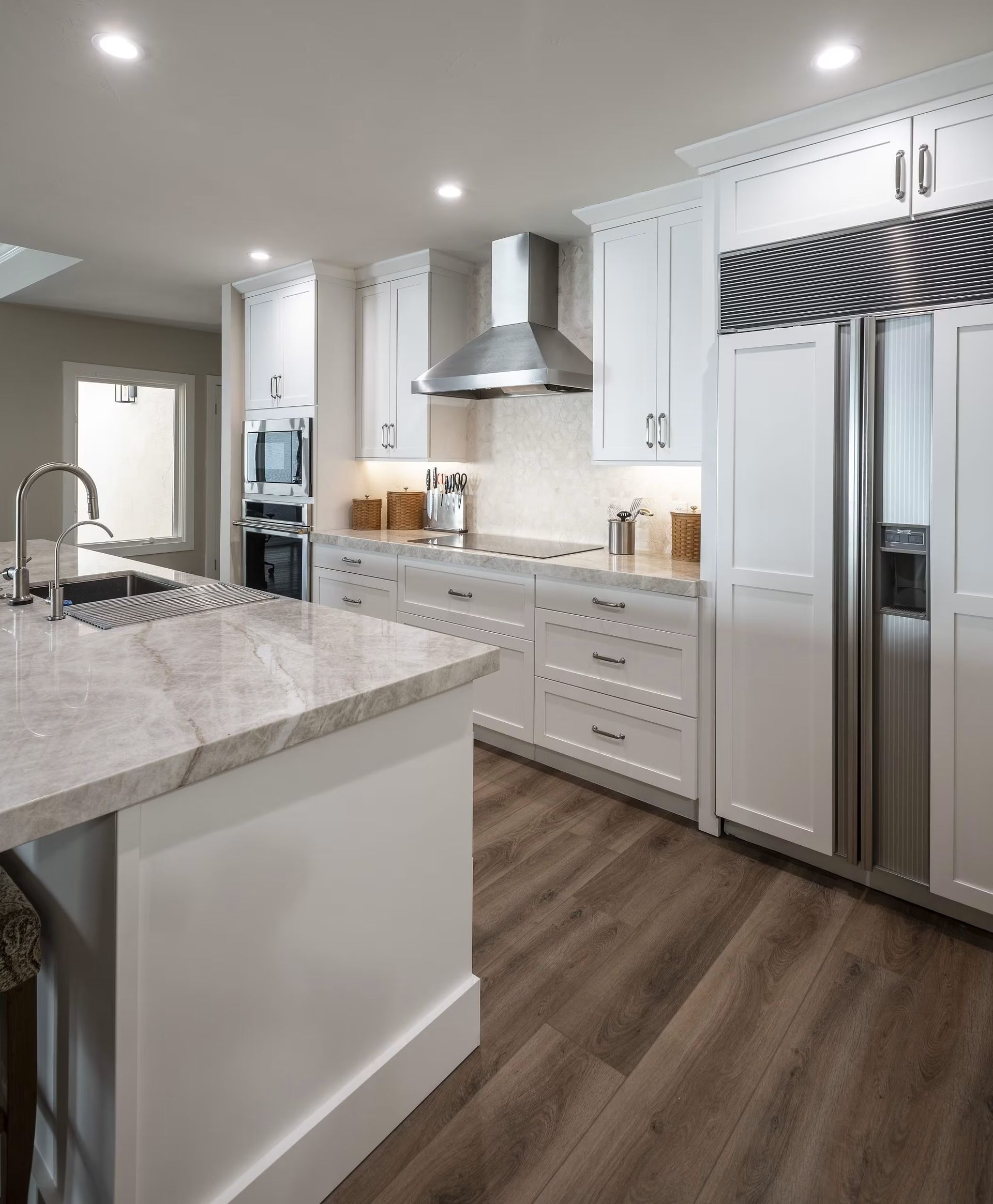 Modern white kitchen with marble island, stainless appliances, and wood flooring