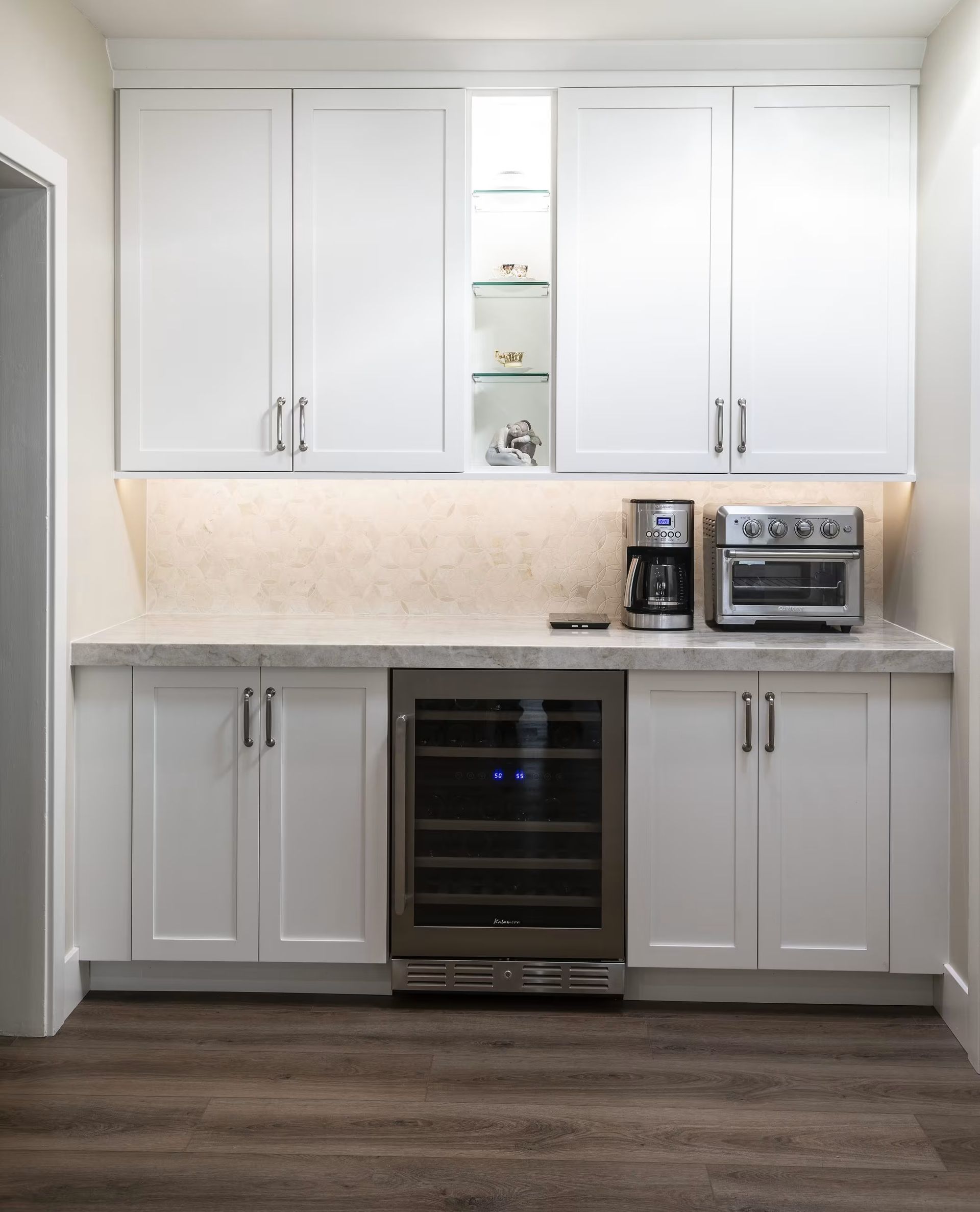 Modern kitchen with white cabinets, gray countertops, stainless wine cooler, and a coffee maker and toaster oven.