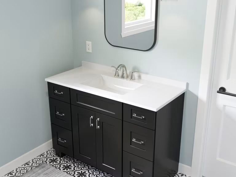 Modern bathroom vanity with black cabinets, white countertop, mirror, and patterned floor tiles