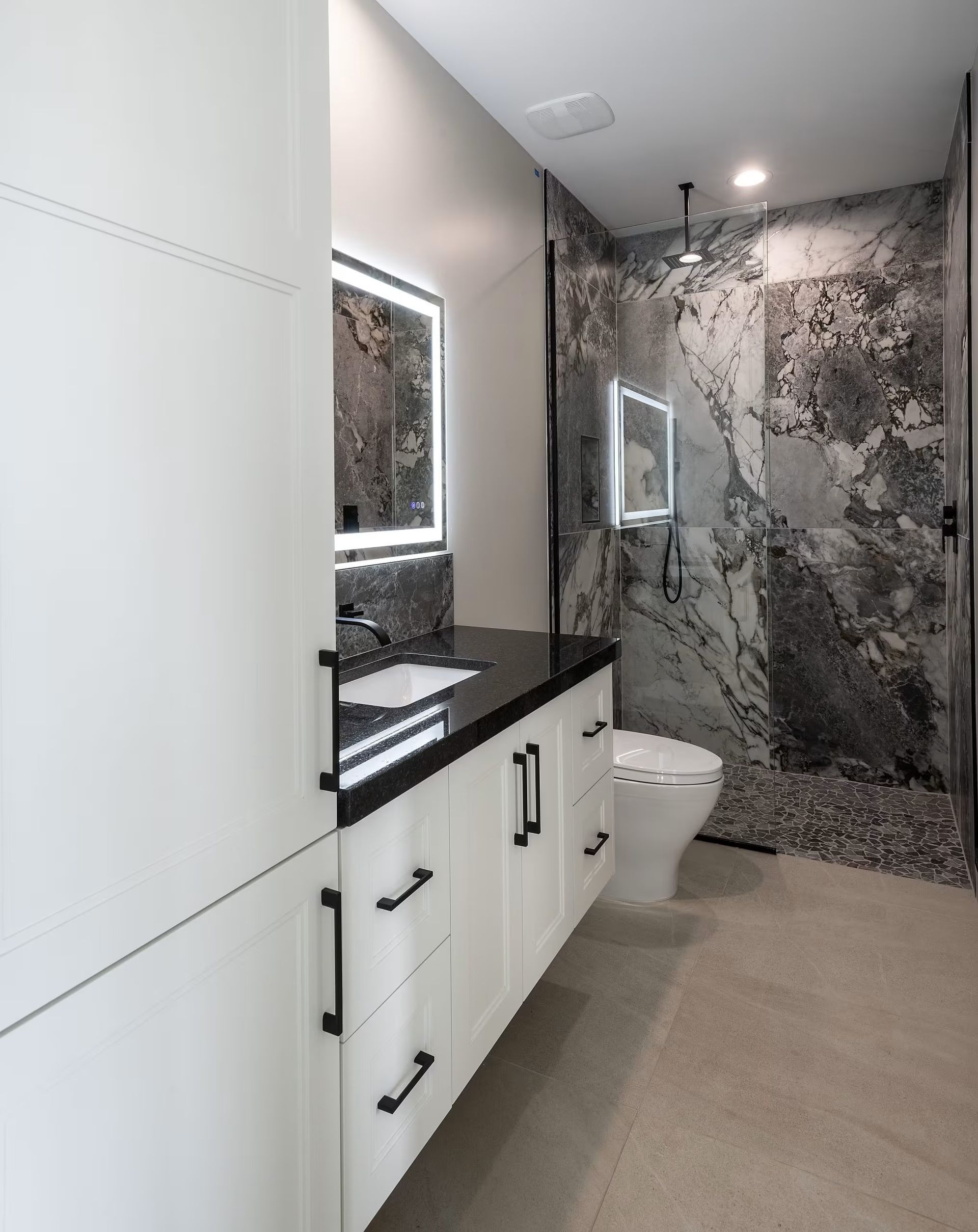 Modern bathroom with white cabinets, black countertop, large mirror, and marble-tiled shower wall.