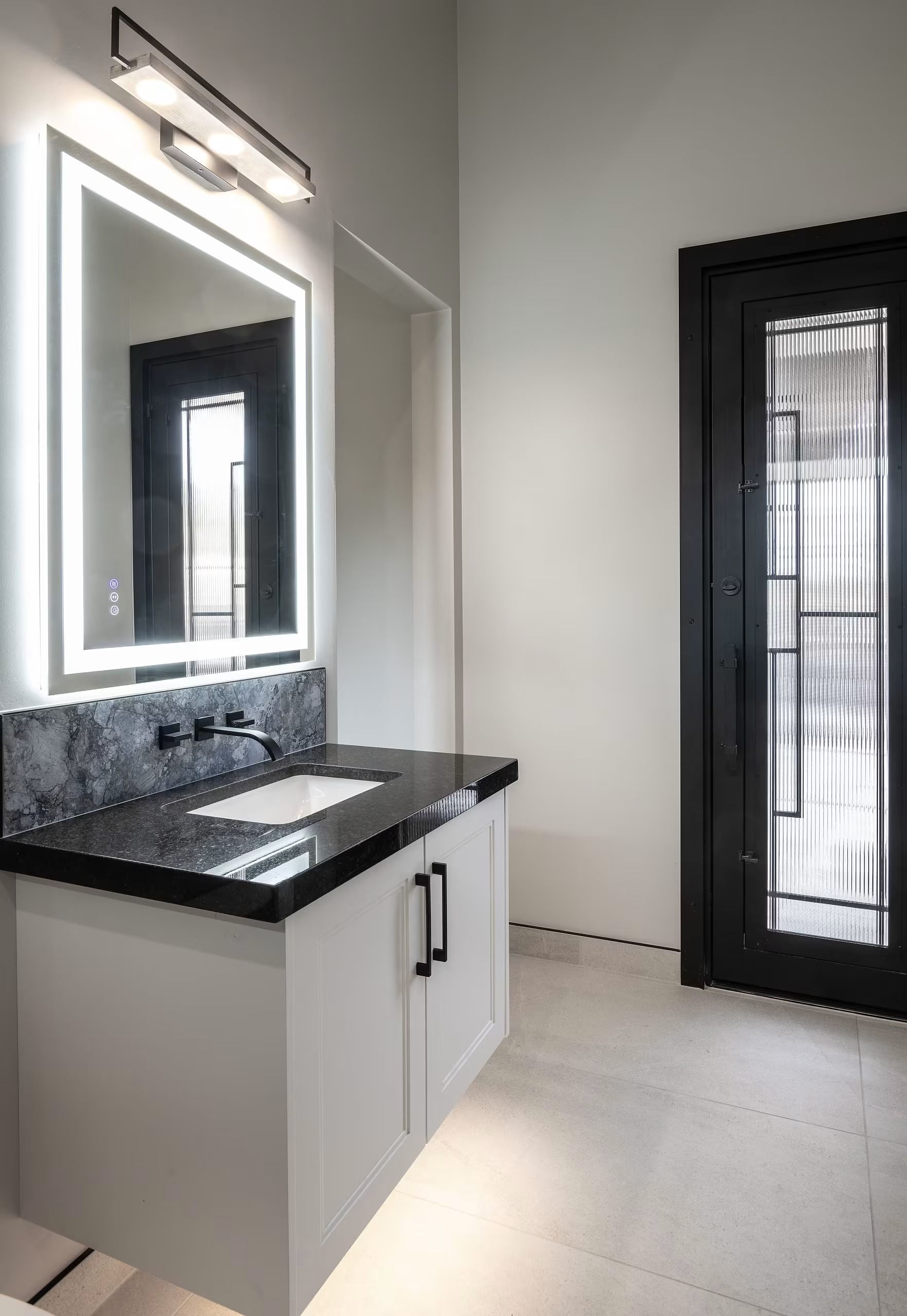 Modern bathroom with a lit mirror, black vanity, and glass shower door