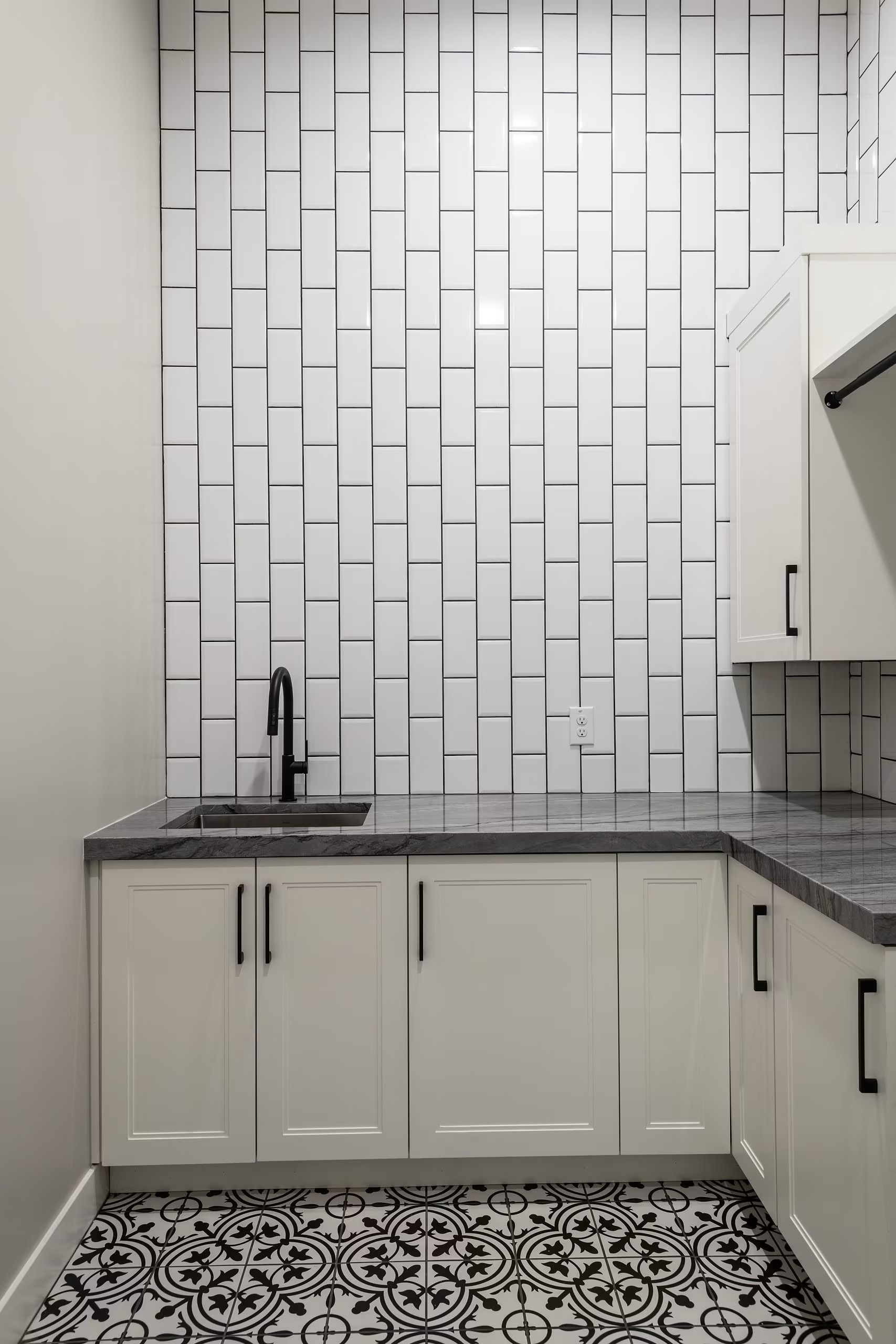 Small white kitchen with geometric tile backsplash, black countertop, and patterned floor tiles.