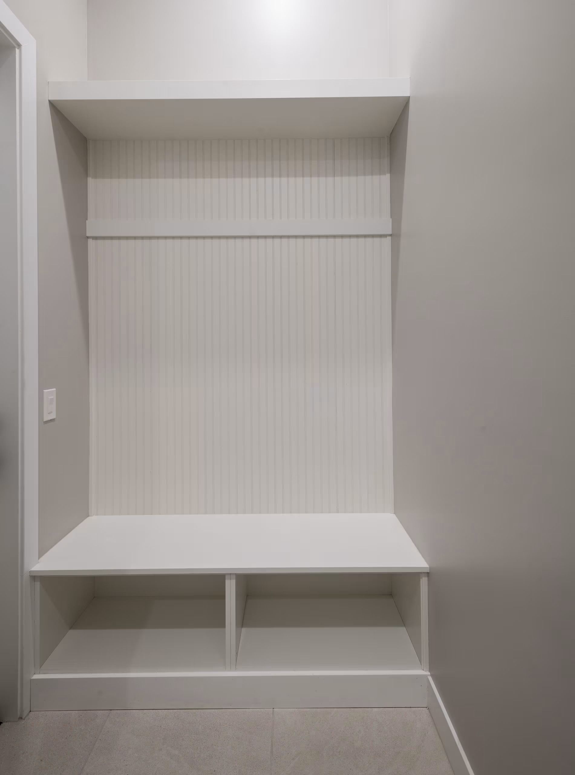 White built-in storage nook with bench seat, vertical beadboard backing, and open cubbies underneath
