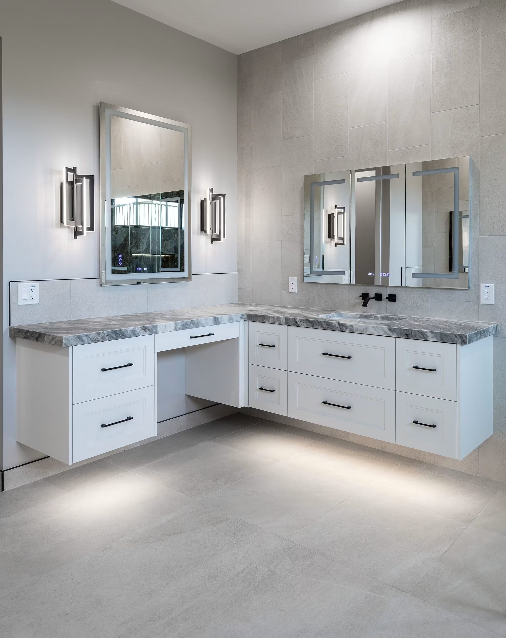Modern bathroom vanity with double sinks, mirrors, wall sconces, and white cabinets in a bright gray room