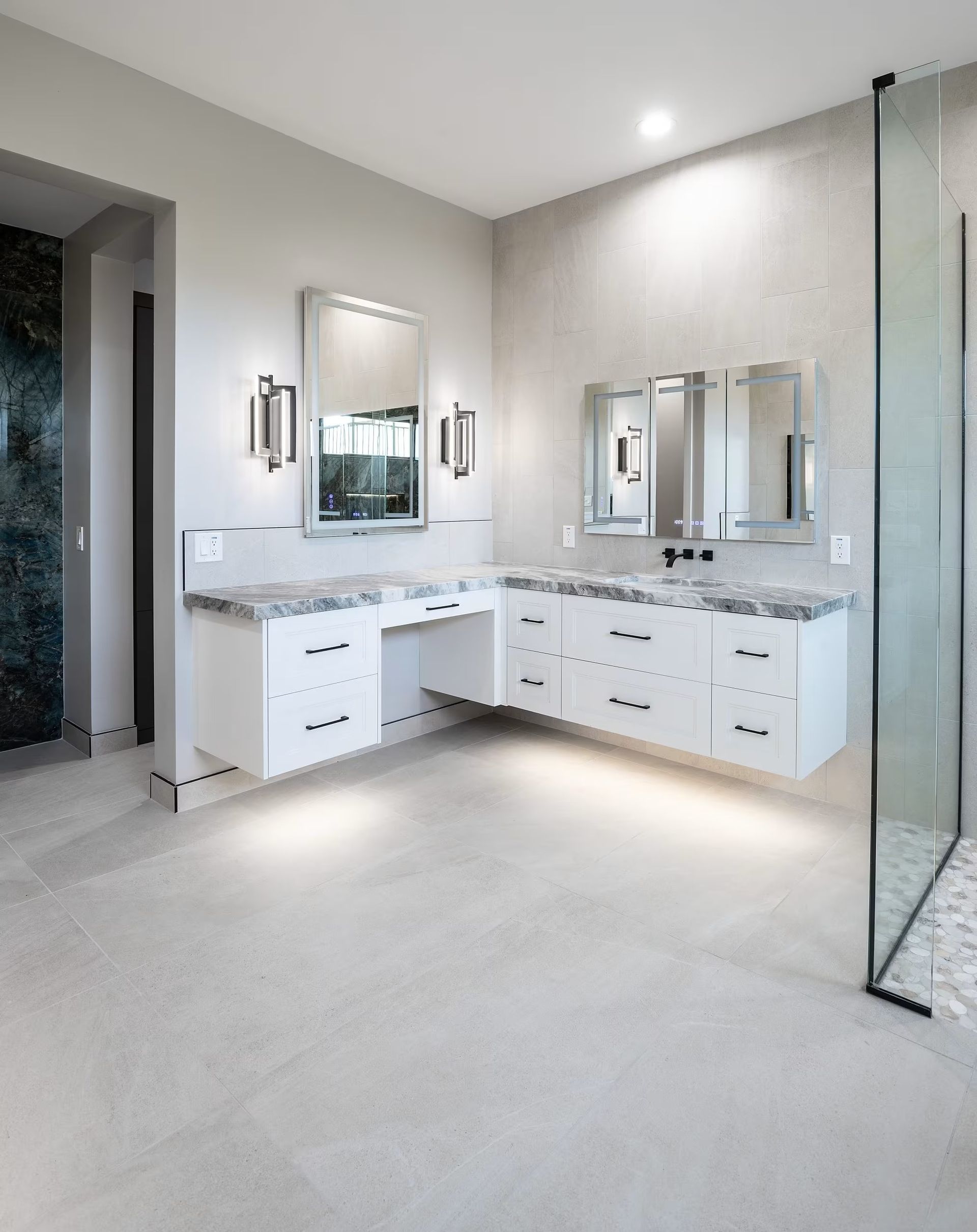 Modern white bathroom vanity with double sinks, mirrors, sconces, and glass shower door