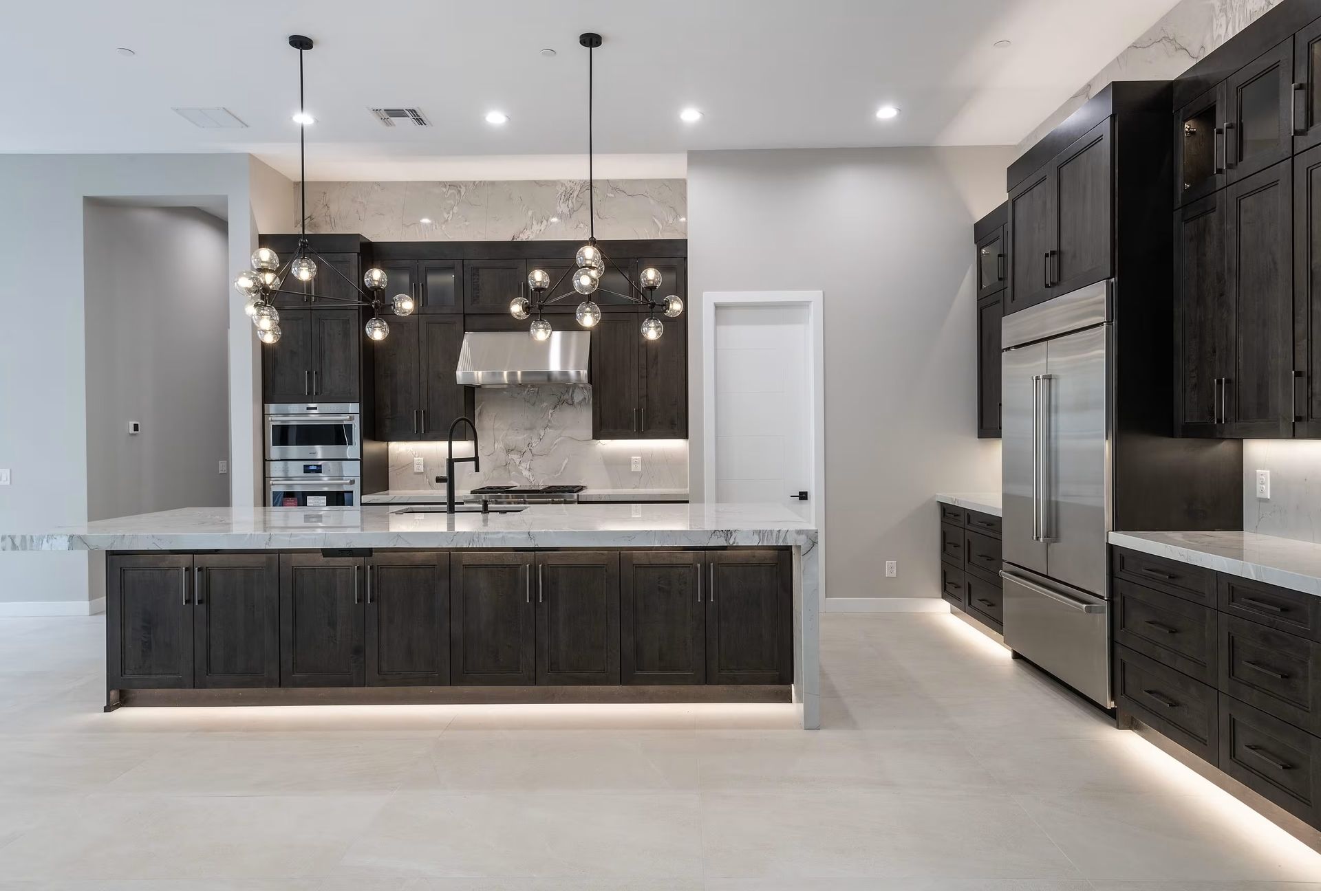 Modern kitchen with dark cabinets, white countertops, stainless appliances, and pendant lighting
