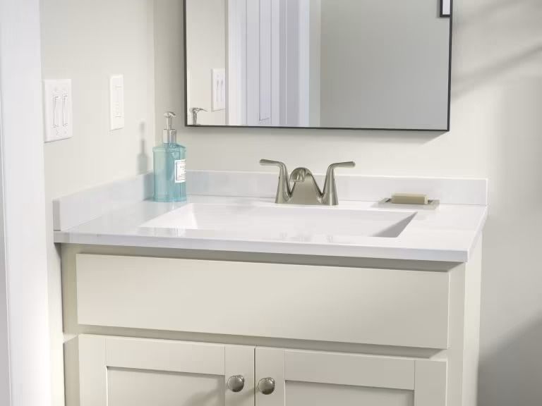 White bathroom vanity with sink, mirror, and soap dispenser near a light-colored wall.