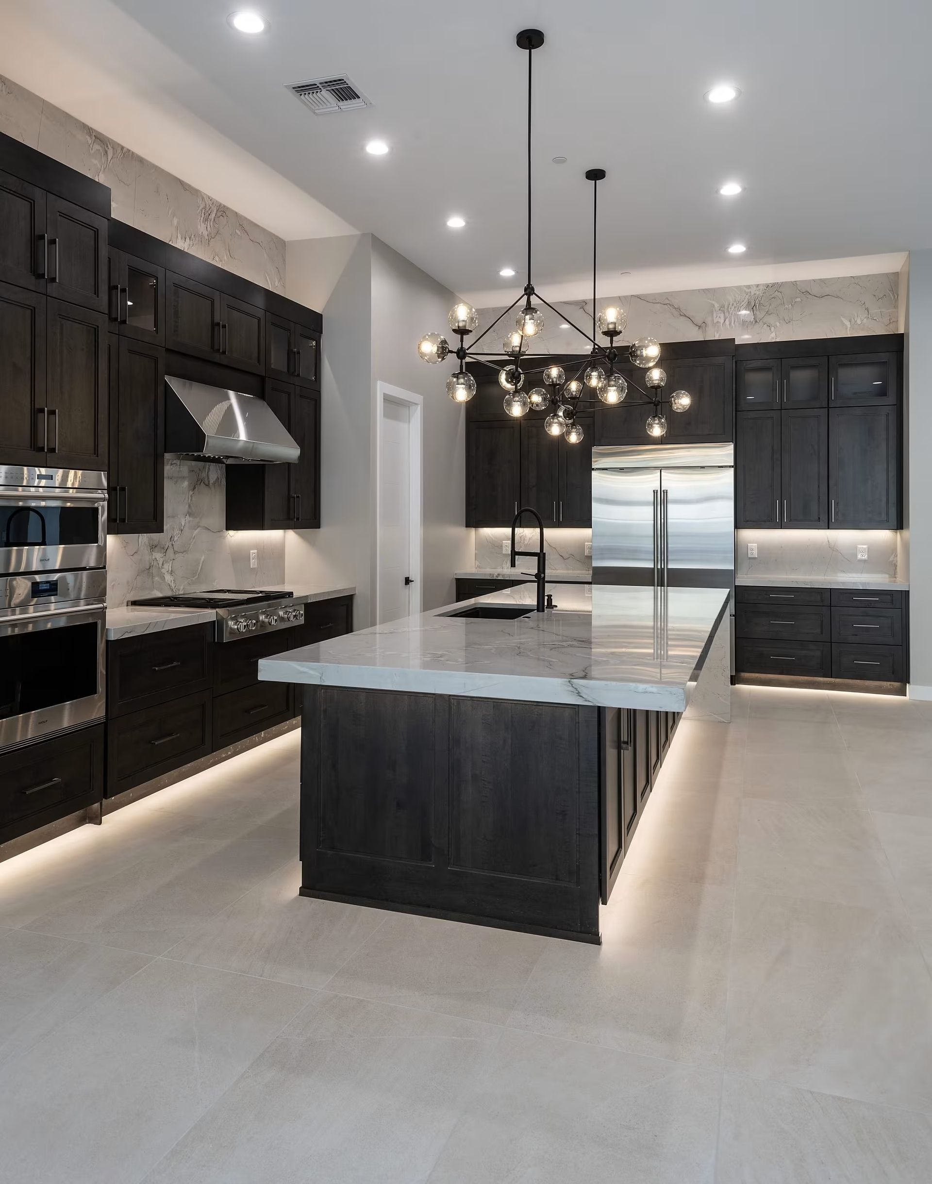Modern kitchen with black cabinets, large island, marble counters, and pendant lights