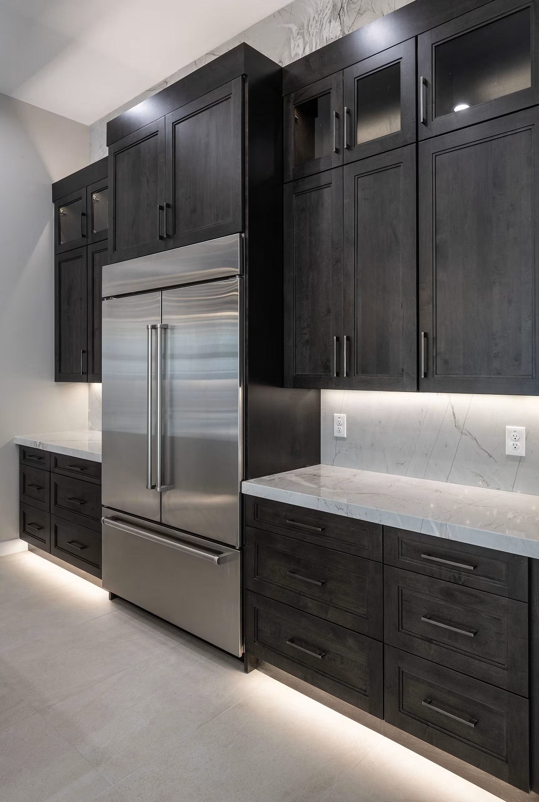 Modern kitchen with dark wood cabinets, stainless steel refrigerator, and light countertops under under-cabinet lighting