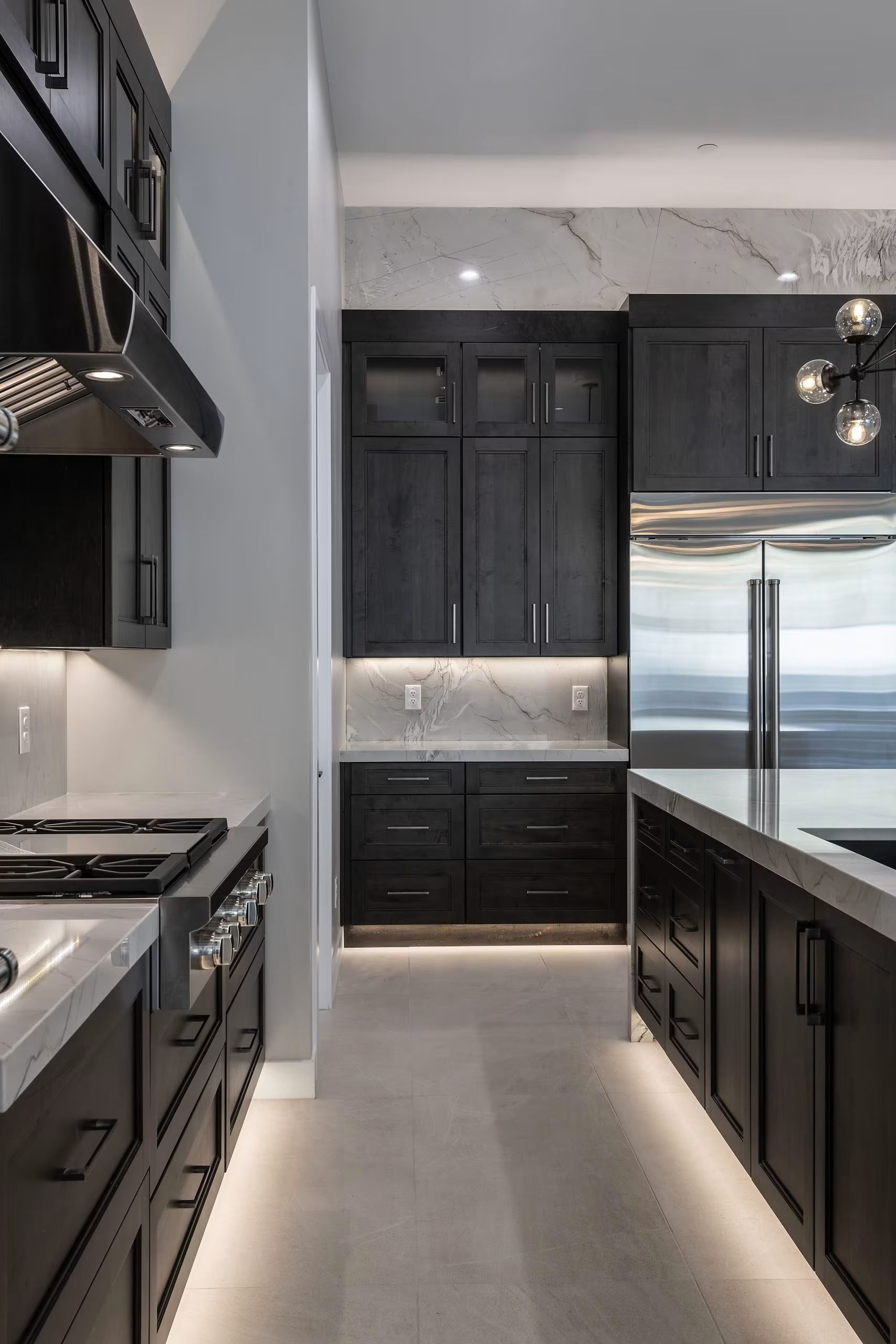 Modern kitchen with dark cabinets, marble countertops, stainless steel appliances, and bright recessed lighting