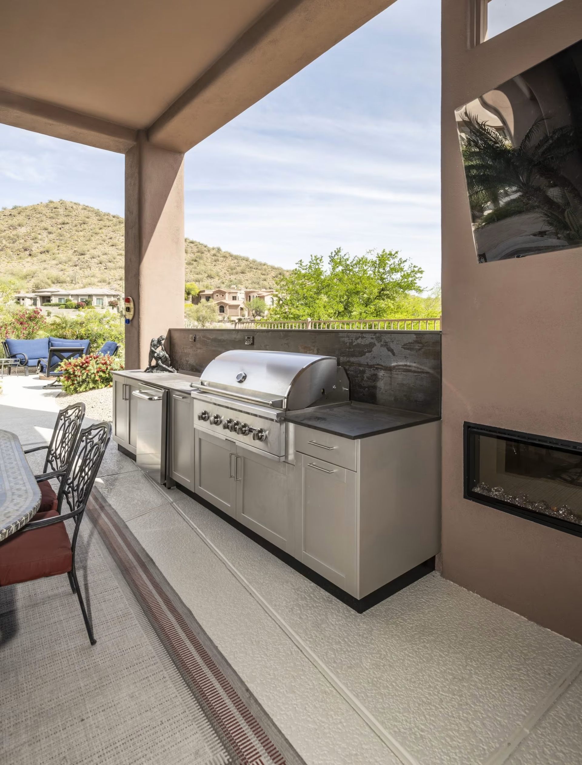Outdoor patio with a built-in stainless steel grill and stone countertop beside a poolside seating area.