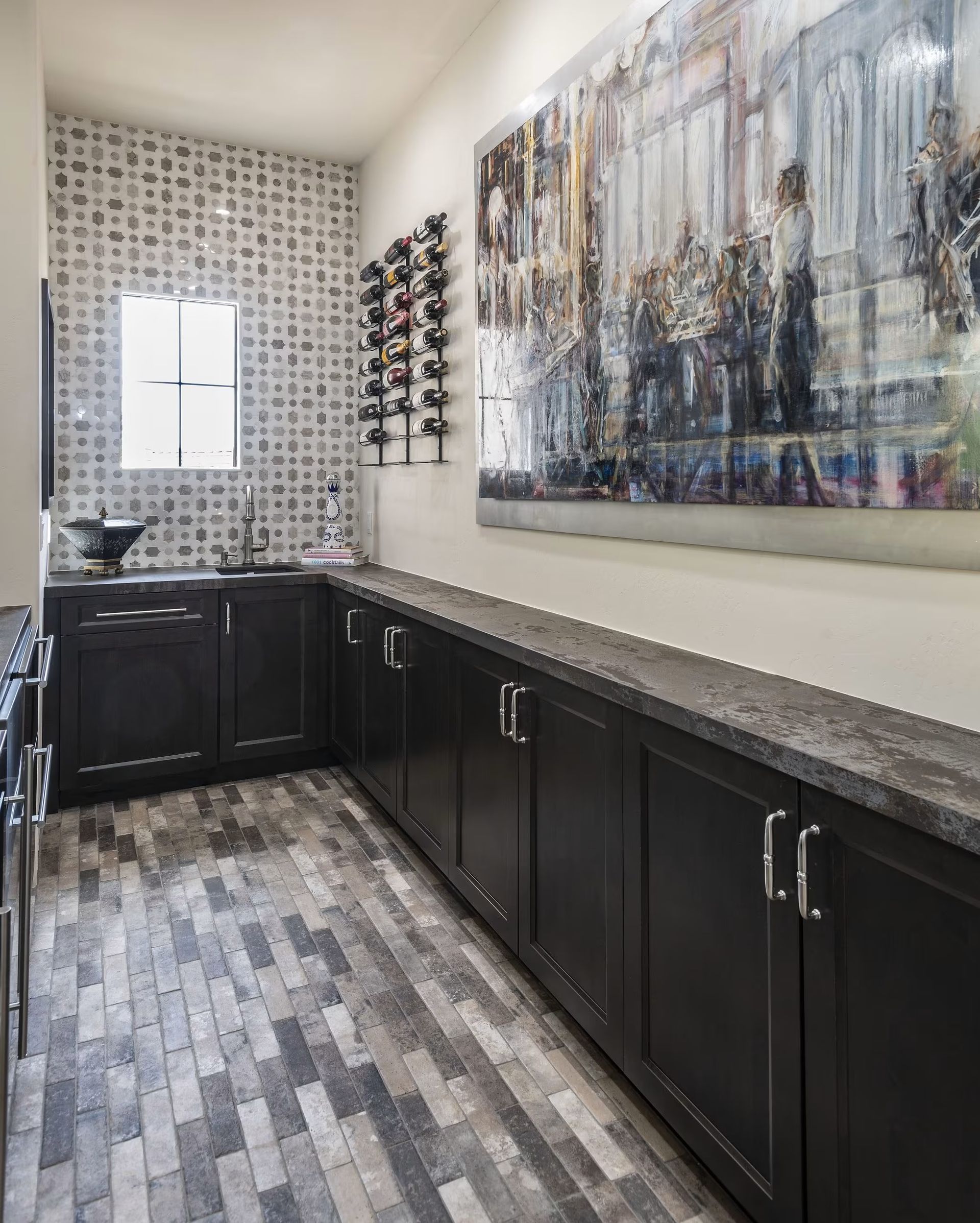 Modern restroom with dark cabinets, stone counters, patterned tile floor, and abstract wall art.
