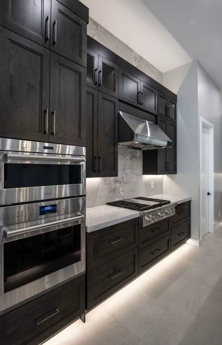 Modern kitchen with dark cabinets, stainless steel appliances, marble backsplash, and gas range under a hood.