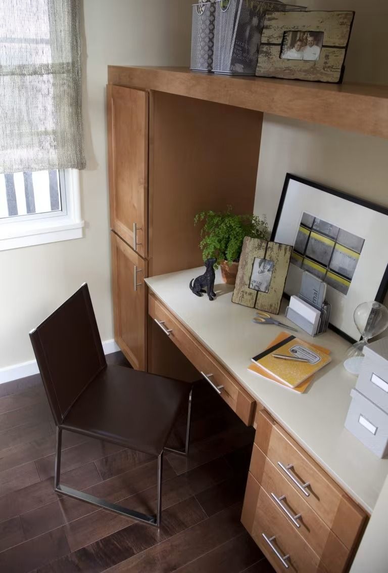 Small home office corner with brown desk, chair, shelves, and papers by a window.