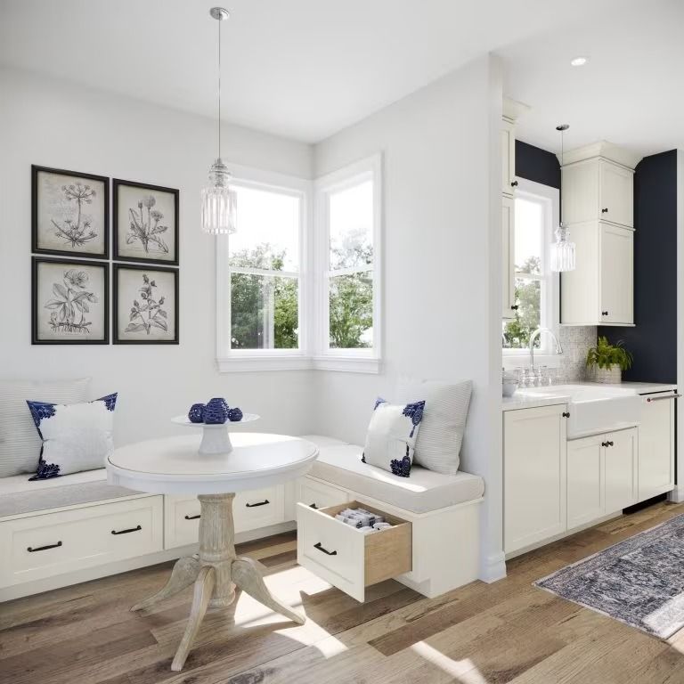 Bright white breakfast nook with built-in bench seating, round table, and adjoining kitchen.
