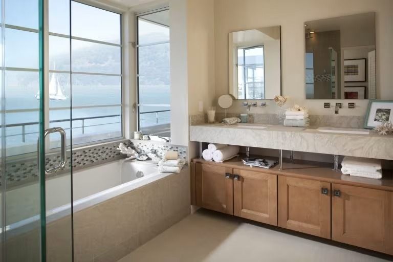 Modern bathroom with a double vanity, large mirror, and ocean-view window beside a bathtub