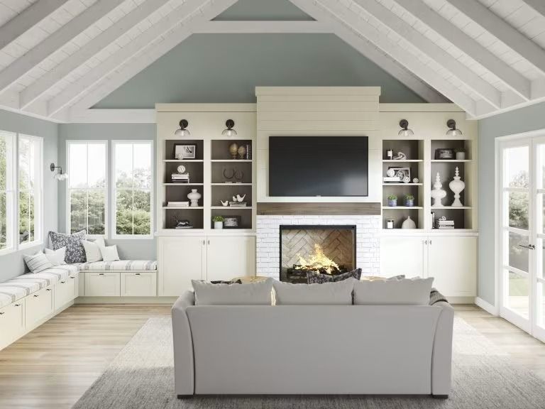 Bright living room with vaulted ceiling, fireplace, built-in shelves, and a gray sofa facing a wall-mounted TV.