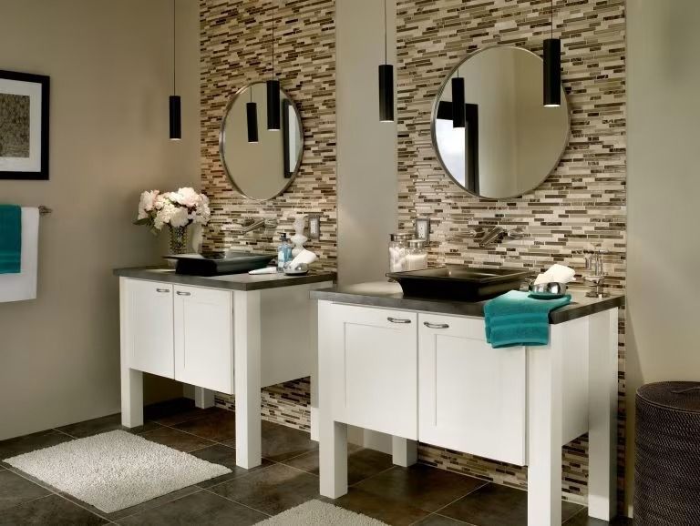Two white vanities with round mirrors in a modern bathroom, one topped with a teal towel and flowers.