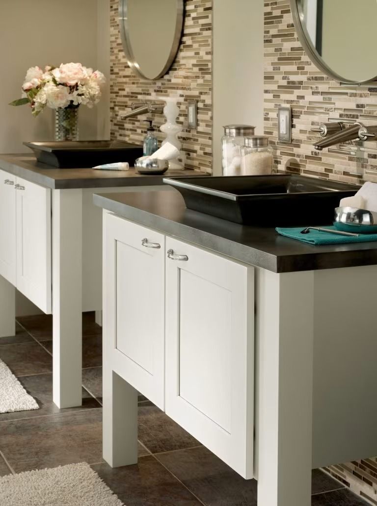 Modern bathroom with double white vanities, black countertops, round mirrors, and stone tile backsplash.