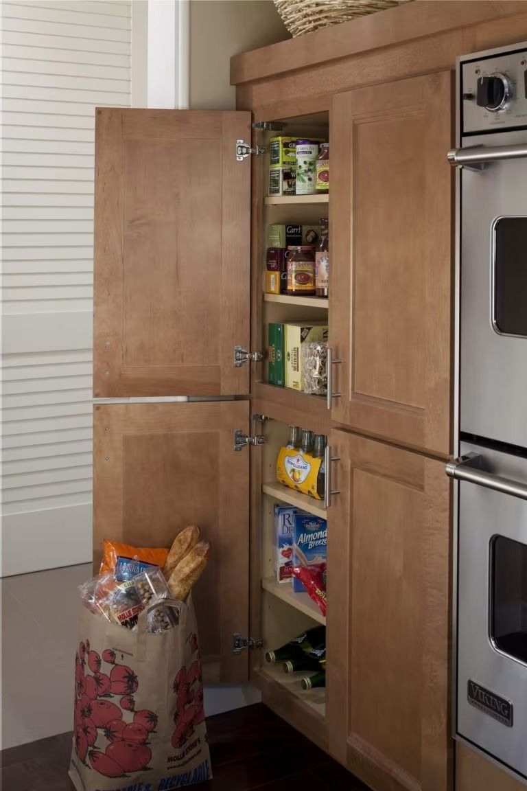 Open pantry cabinet with shelves of canned and boxed food next to kitchen ovens
