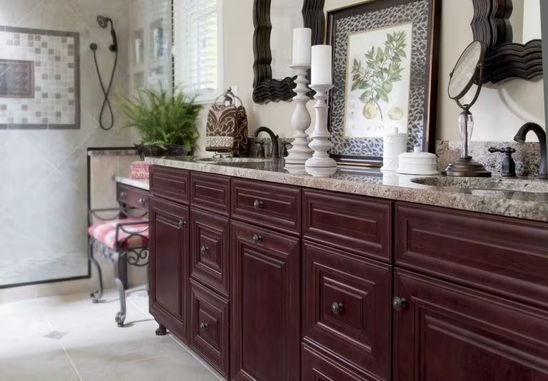 Elegant bathroom vanity with dark wood cabinets, granite countertop, mirrors, and white candles.