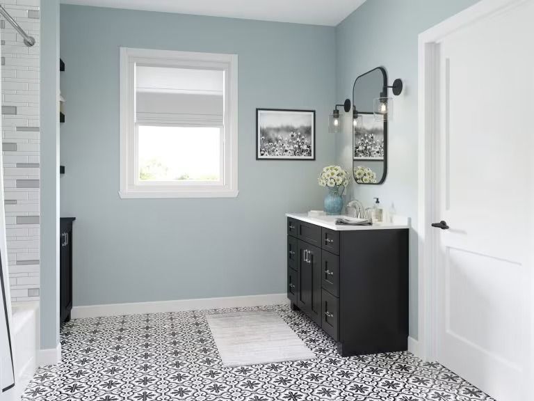 Modern bathroom with patterned tile floor, light blue walls, black vanity, and white shower curtain