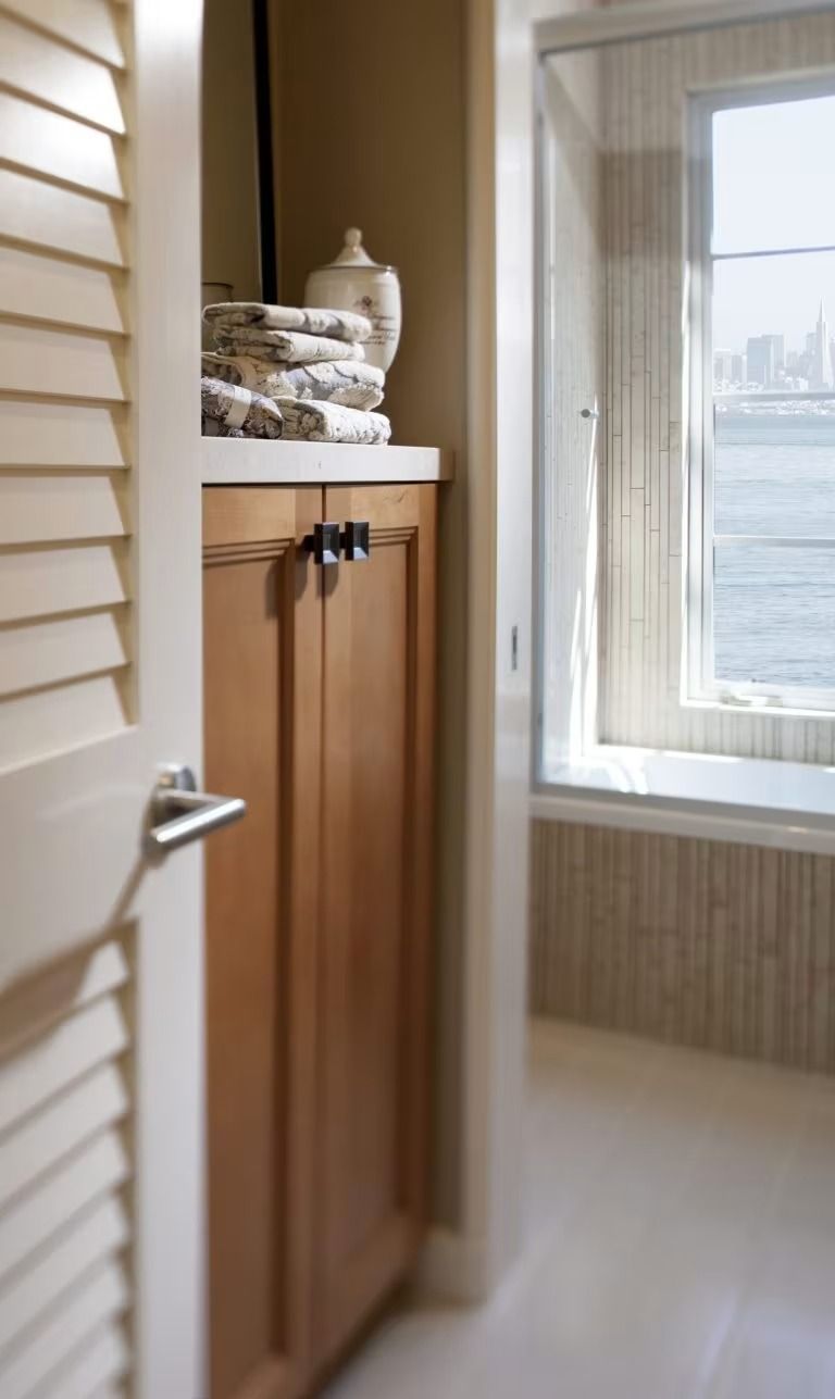 Small bathroom with wood cabinet, folded towels, and a window overlooking water and distant buildings