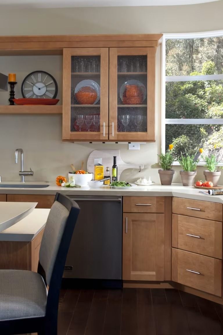 Modern kitchen with wood cabinets, dark island seating, sink, and potted plants by a bright window