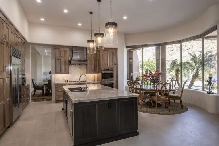 Spacious modern kitchen with island, pendant lights, and bay-window dining nook with palm views