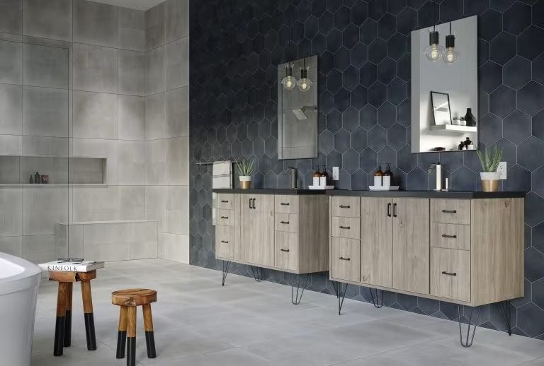 Modern bathroom with gray tiled walls, wood vanities, black counters, mirrors, and stools near a tub