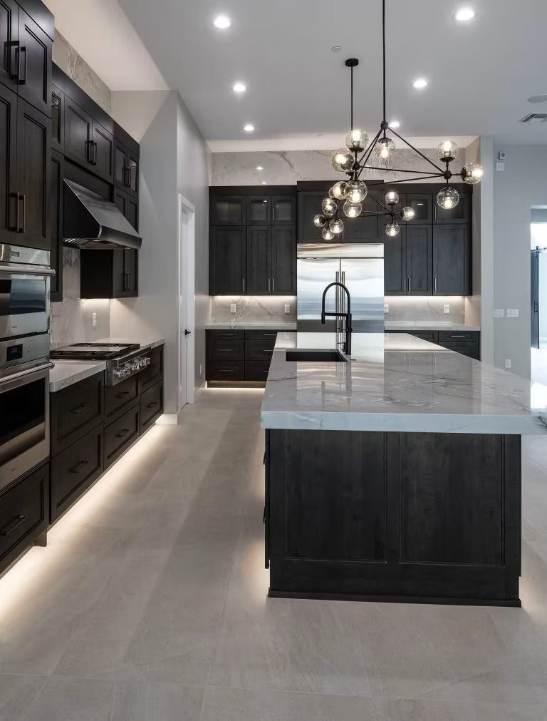 Modern luxury kitchen with dark cabinets, marble island, pendant lights, and light gray flooring