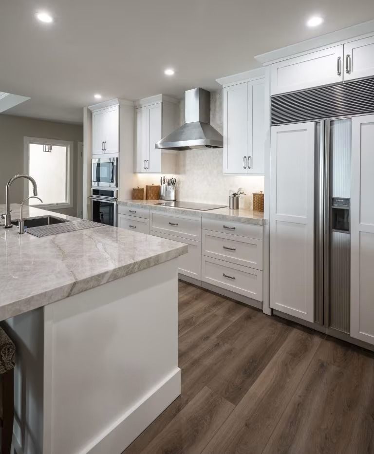 Modern white kitchen with marble island, stainless appliances, and wood flooring