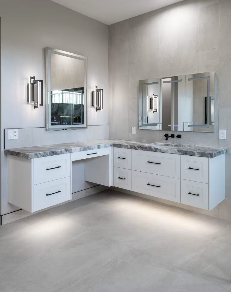 Modern bathroom vanity with white cabinets, gray marble countertop, and mirrored wall sconces under soft lighting