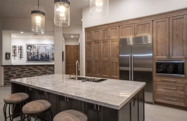Modern kitchen with large island, marble countertop, barstools, wood cabinets, and stainless steel appliances