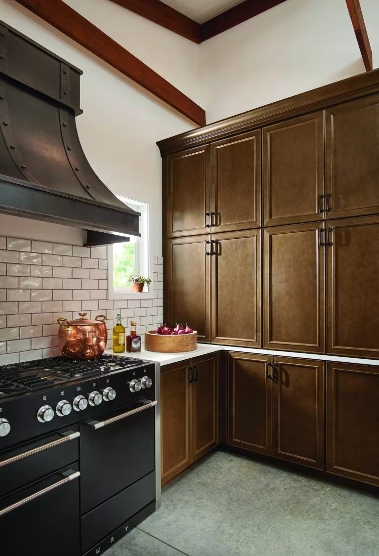 Kitchen with black stove and hood, white tile backsplash, and large wooden cabinets in a rustic interior.
