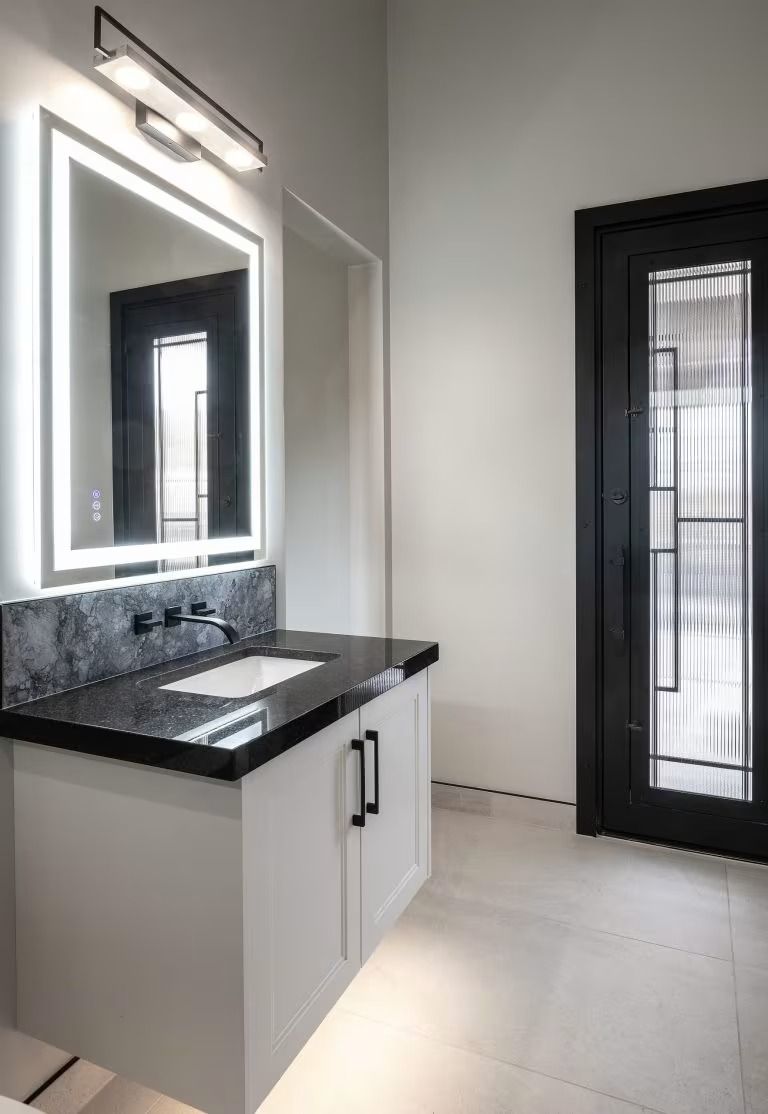 Modern bathroom with a lighted mirror, black countertop sink, and frosted glass door