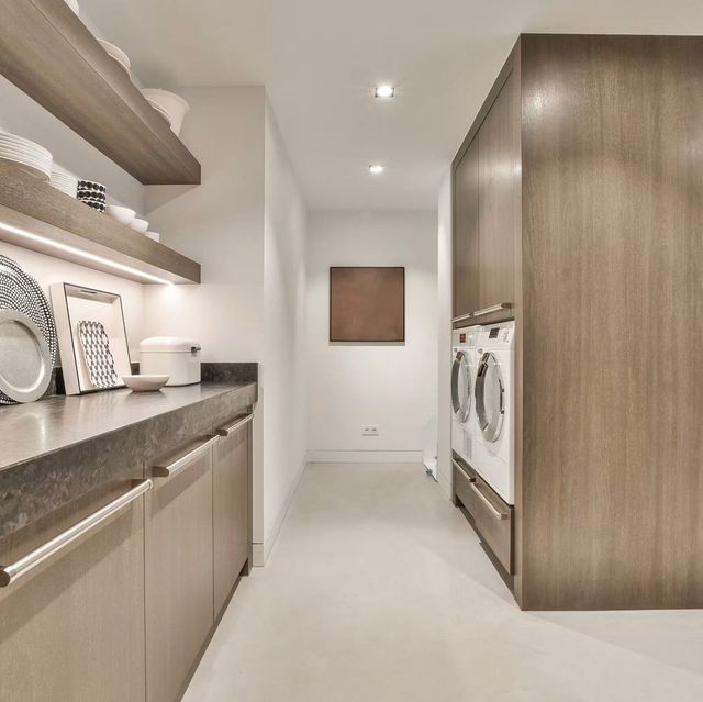 Bright laundry room with wood cabinets, shelves, and front-loading washer and dryer.