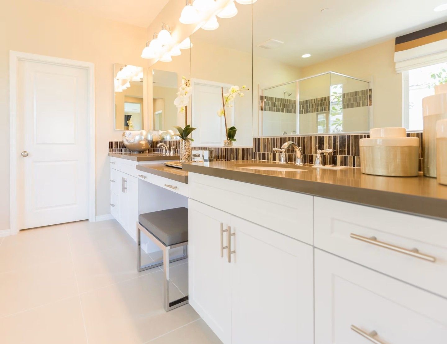 Bright modern bathroom vanity with white cabinets, large mirror, and beige countertop under warm lighting