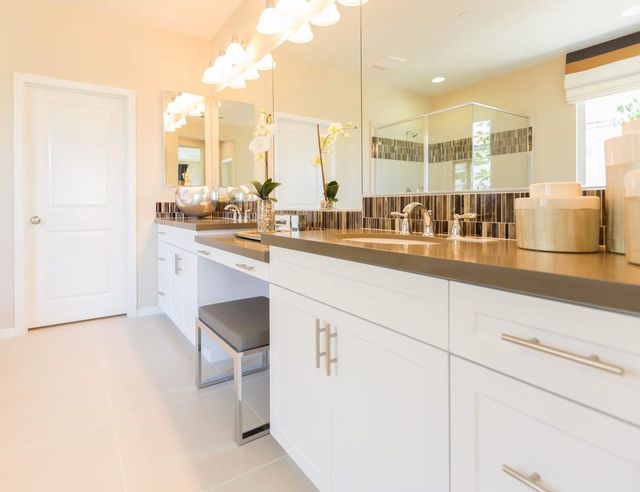 Bright bathroom with white cabinets, long mirror, marble countertop, and gold fixtures.