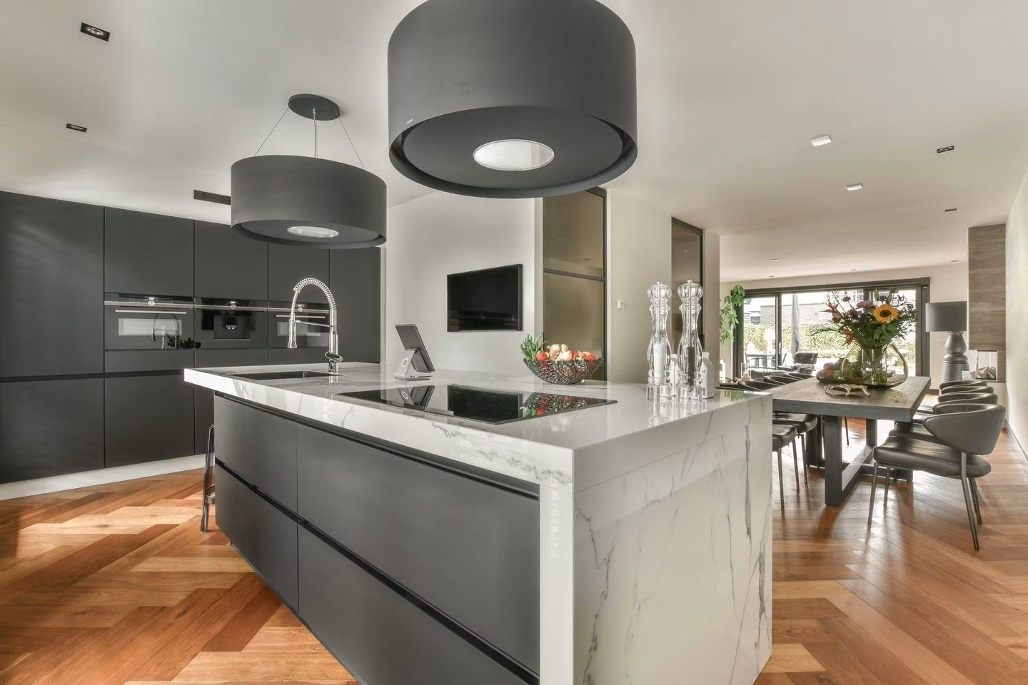 Modern open-plan kitchen with black cabinetry, white marble island, wood floors, and dining area beyond