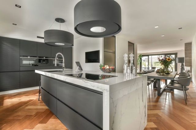 Modern open kitchen with dark cabinets, white island, black pendant lights, and wood floors