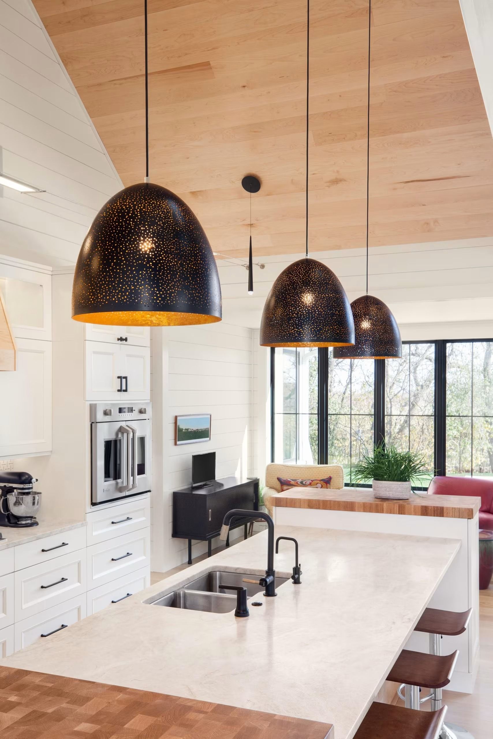 Modern kitchen with large island, black pendant lights, white cabinets, and a bright window seat