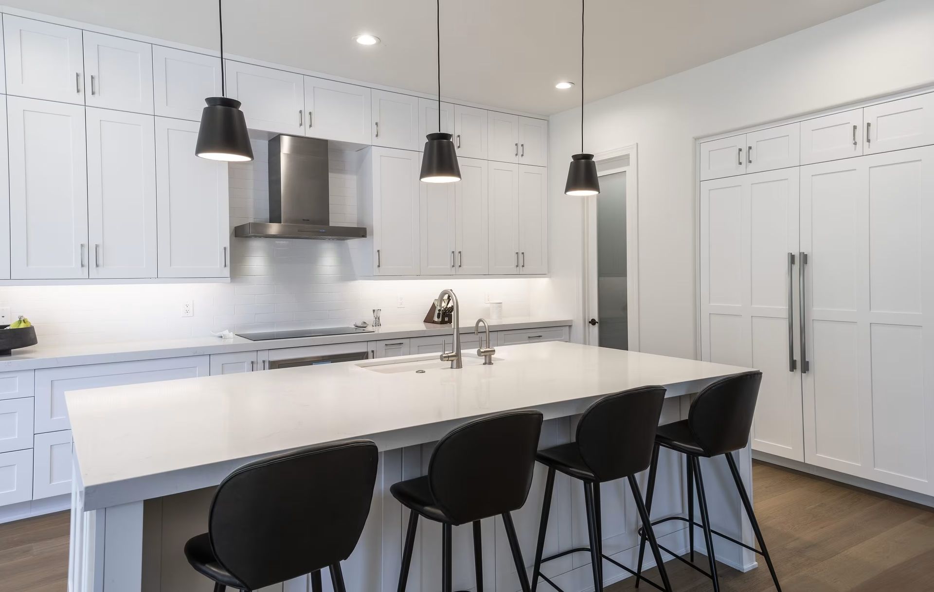 Modern white kitchen with island, black pendant lights, and black stools