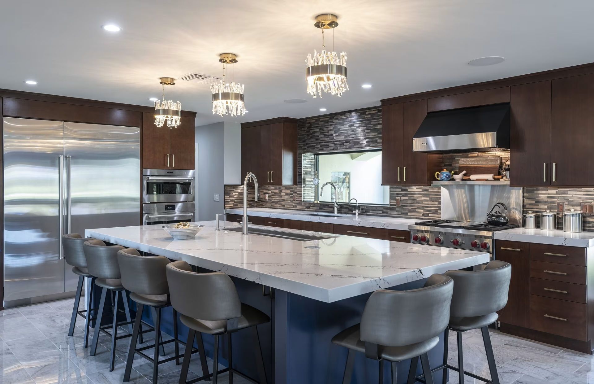 Modern kitchen with large marble island, dark wood cabinets, stainless steel appliances, and pendant lights