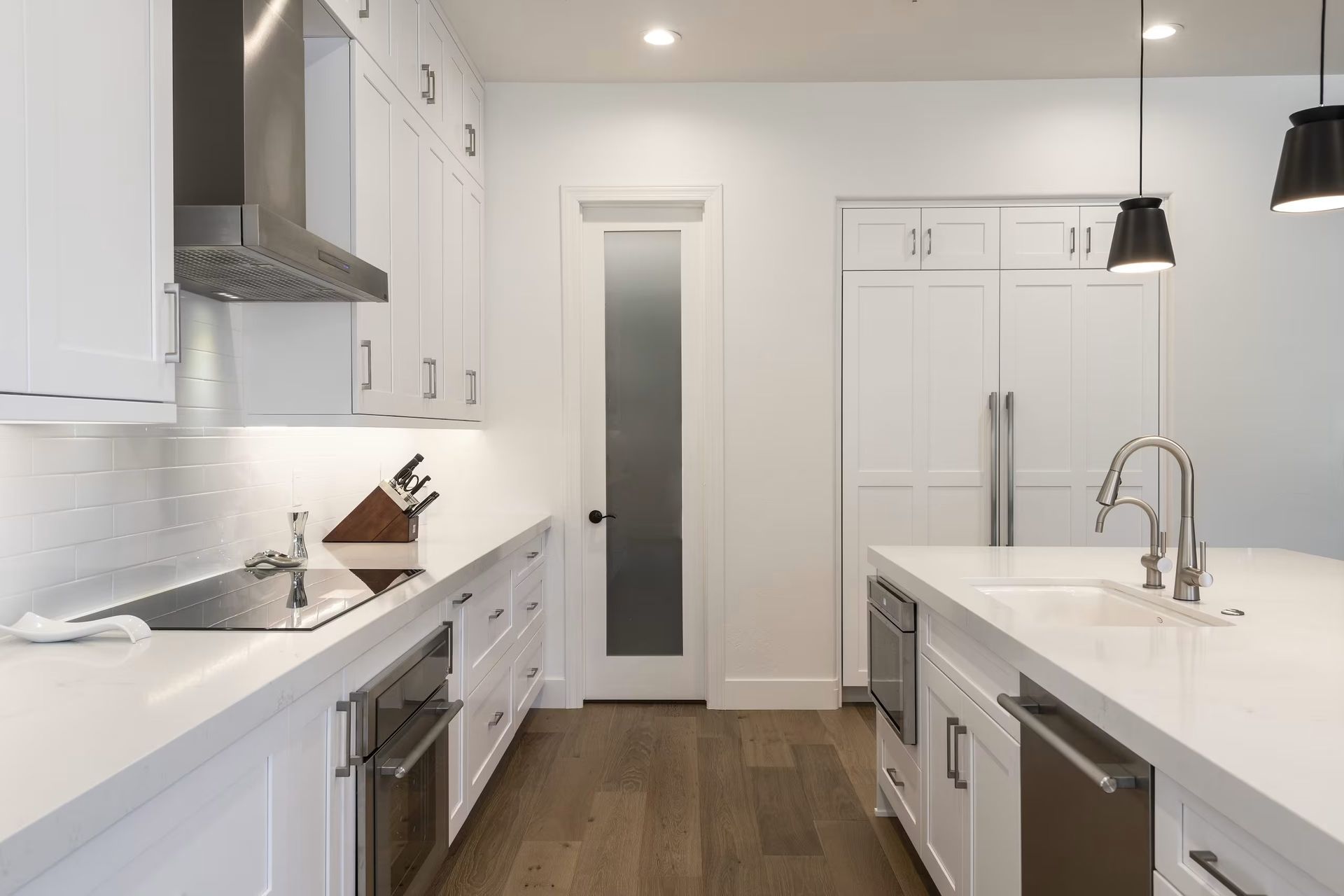 Modern white kitchen with stainless steel appliances, island sink, and wood flooring.