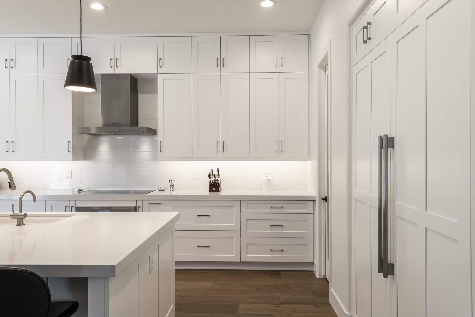 Bright white modern kitchen with island, stainless range hood, and tall pantry cabinets