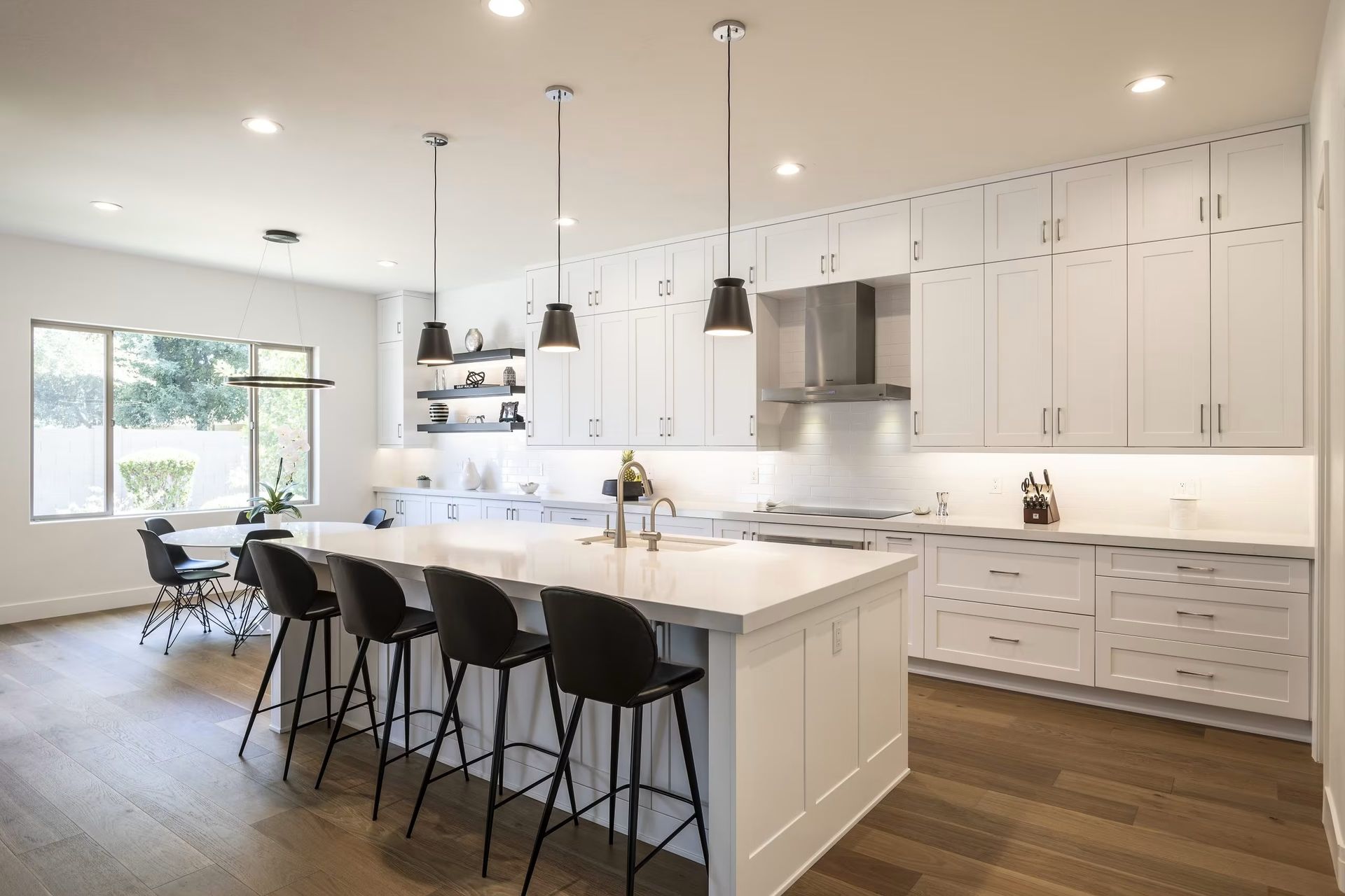 Bright white modern kitchen with island, black barstools, pendant lights, and wood floors