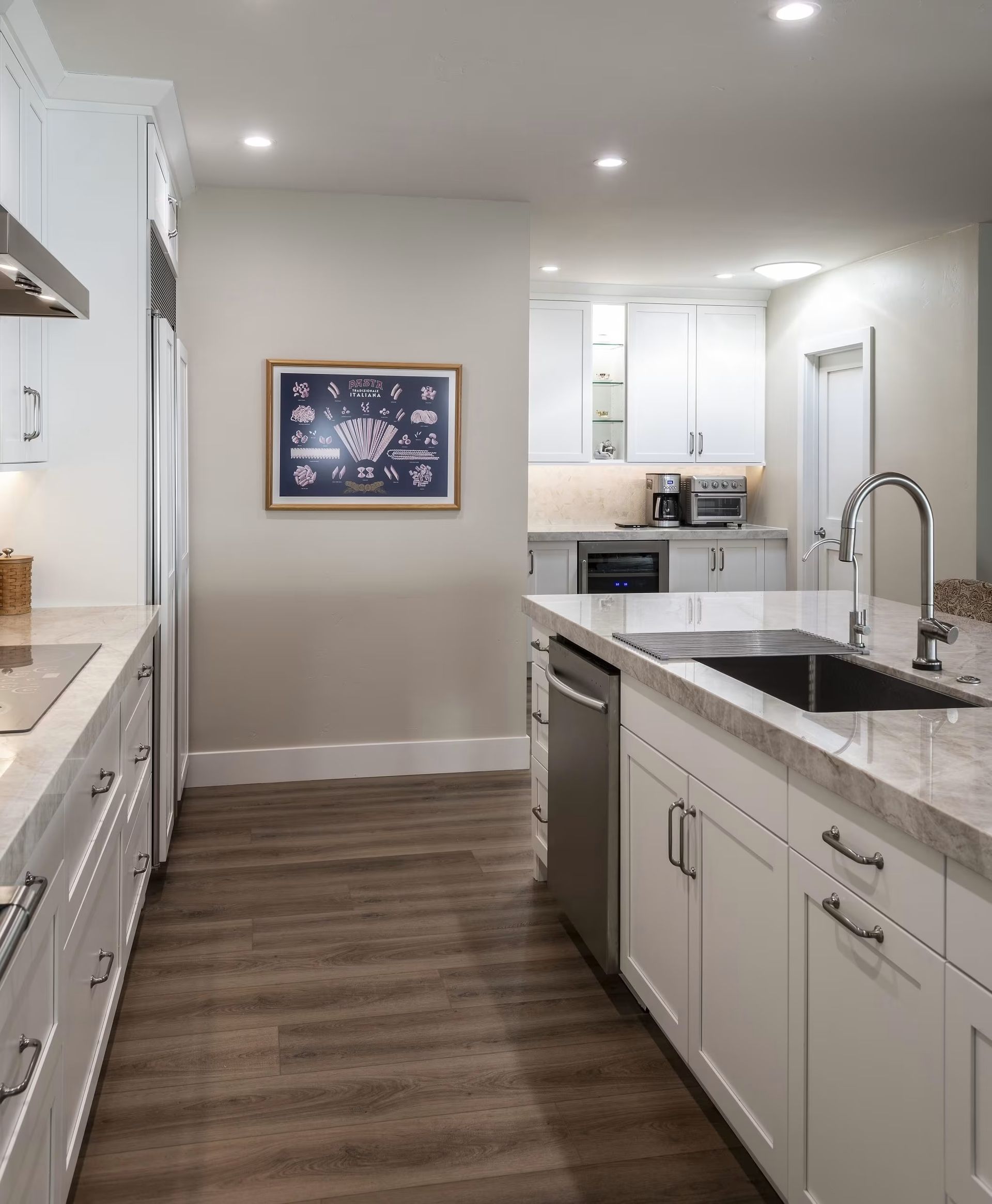 Bright modern kitchen with white cabinets, marble island, stainless sink, and wood-look flooring
