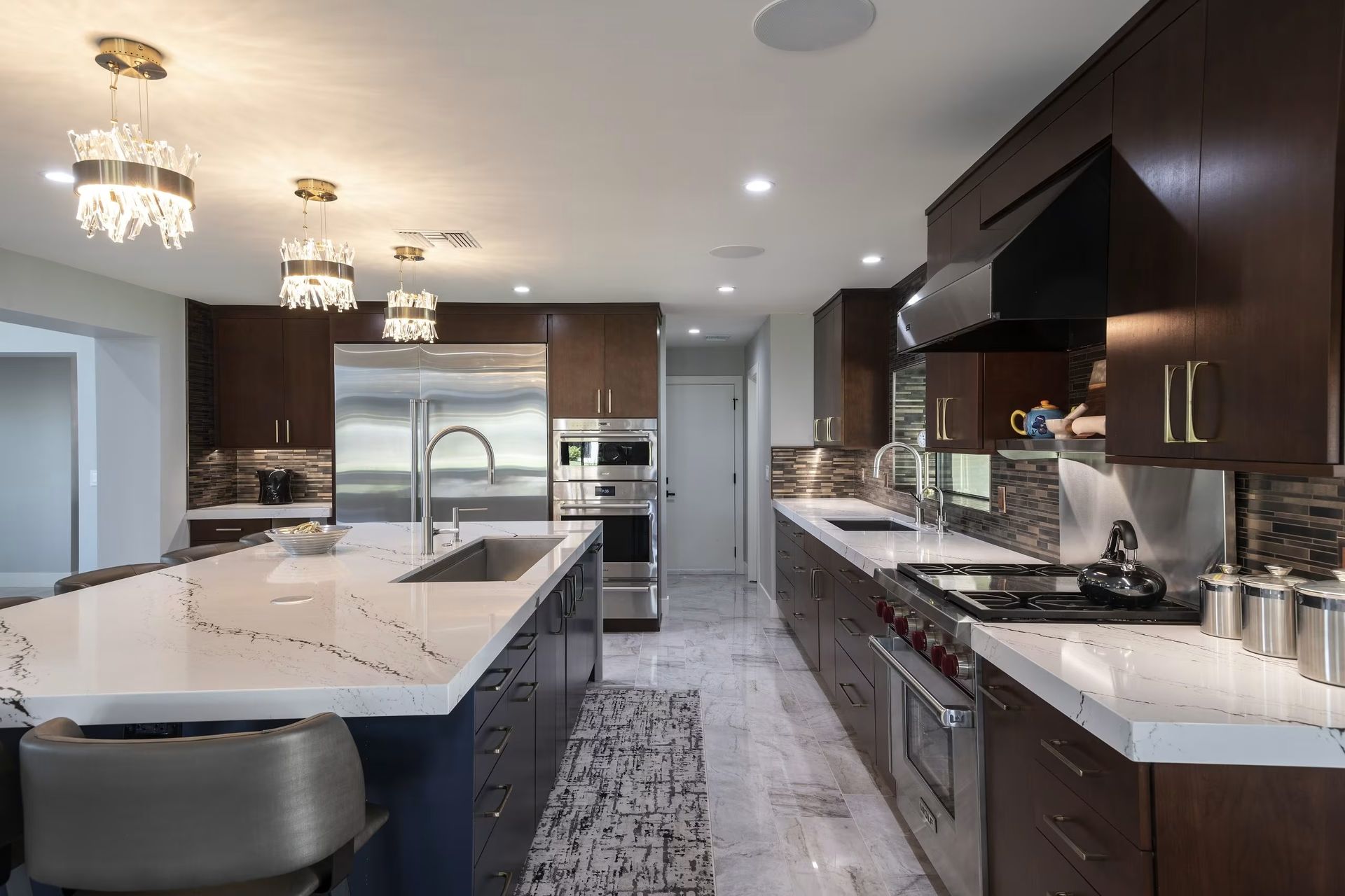 Modern kitchen with large island, marble countertops, stainless steel appliances, and dark wood cabinets