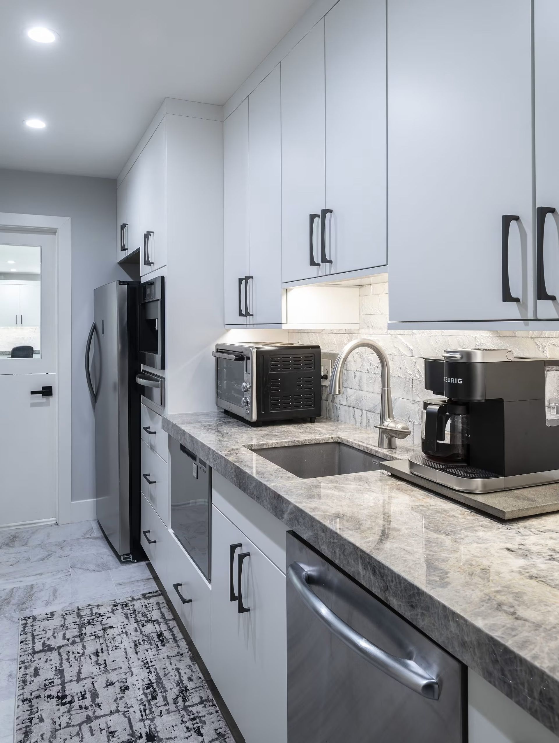 Bright modern kitchen with white cabinets, granite countertops, stainless appliances, and a patterned runner rug